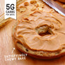 Low carb Bagel with peanut butter spread on a wooden surface, with text indicating low carb content and texture.
